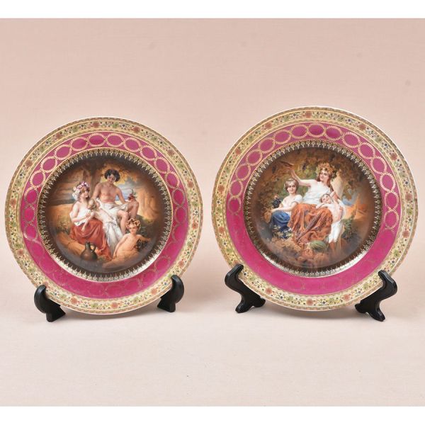 Par de pratos decorativos em porcelana tcheca, ricamente ornamentados com reservas centrais reproduzindo cenas galantes e alegóricas de inspiração neoclássica, com figuras femininas, putti e personage