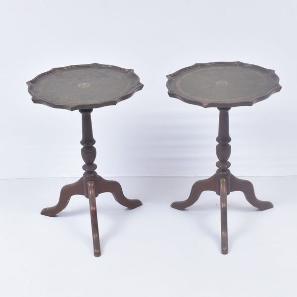 Par de mesas em madeira nobre entalhada, estilo inglesa com tampo circular recortado em formato `pie crust` em couro pirogravado. Fuste central torneado, com sucessão de balaústres e anéis, apoiado so