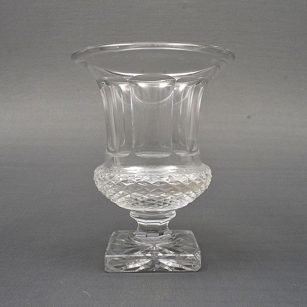 Vaso europeu em cristal lapidado, de formato campanular sobre pedestal quadrangular. Corpo decorado com caneluras verticais e faixa central lapidada em padrão geométrico, destacando-se pela ampla boca