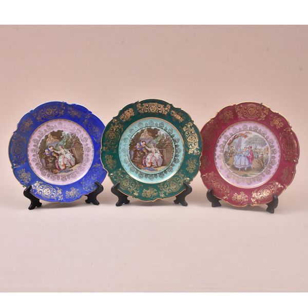Conjunto de três pratos de celeção em porcelana alemã da Bavária, cada um emoldurado por abas com rica decoração floral dourada e fundo de cor distinta — azul cobalto, verde esmeralda e magenta — circ