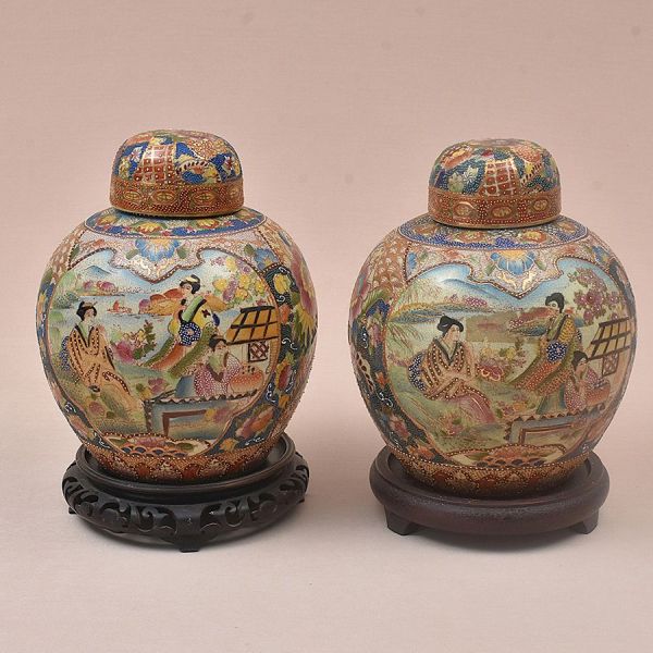 Par de potiches japonesas com tampa, em porcelana finamente decorada em estilo Satsuma, com fundo em reticulado dourado e cartelas reservadas pintadas com cenas de gueixas em jardins floridos, emoldur