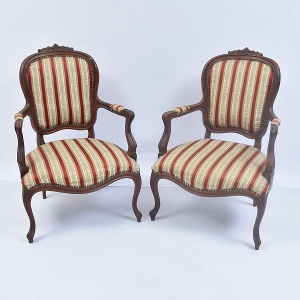Par de poltronas (fauteuils) em estilo Luís XV, em madeira entalhada com espaldar em medalhão encimado por arranjo floral. Os braços são recortados em curva, com apoia-braços estofados e terminando em