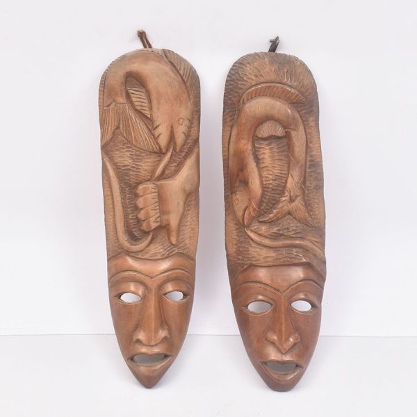 Par de máscaras africanas esculpidas em madeira, apresentando rostos estilizados de feições alongadas, olhos vazados e bocas abertas, características comuns da arte tribal africana. As peças são ricam