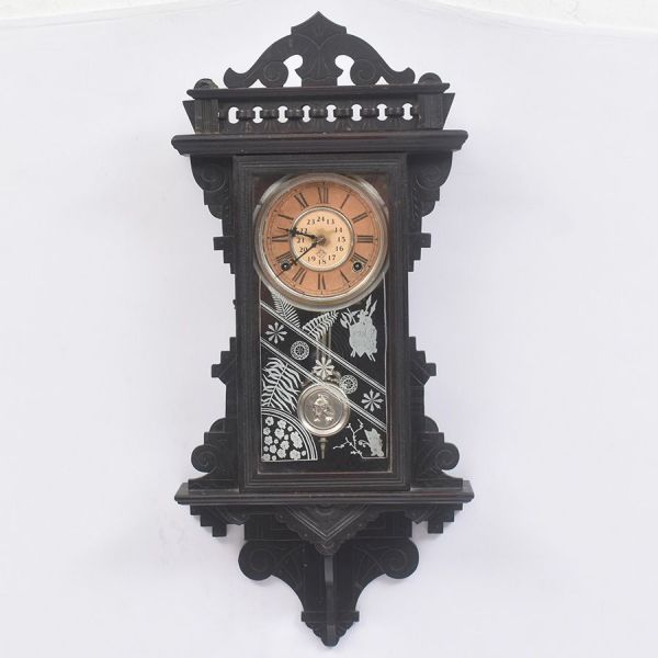 Relógio de parede americano, manufatura Relógio de madeira, dito oito, da casa Ansonia Clock em madeira ebanizada, com friso vazado no coroamento e cornija recortada. Porta inferior em vidro pintado c