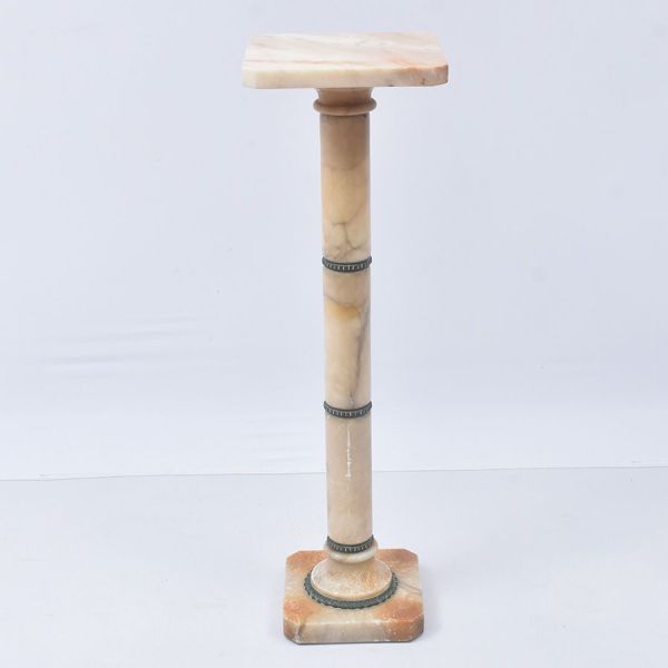 Coluna-pedestal em alabastro, de seção quadrangular, composta por tampo e base em tons mesclados de creme e mel, sustentados por fuste cilíndrico igualmente em alabastro. Apresenta delicados anéis dec
