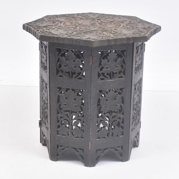 Mesa de base oitavada articulada, em madeira entalhada e patinada em tom escuro. Formada por oito painéis dobráveis com entalhe vazado de folhagens de parreiras. Tampo octogonal com mesmo padrão flora