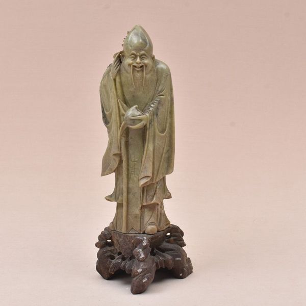 Estatueta de pedra sabão na cor verde representando Shou Xing, o deus da Longevidade. Segura o pêssego e traz o cajado feito de também ramos de pessegueiro representam a divindade da Longevidade. Caja