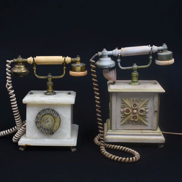 Dois telefones estilo vintage: um com corpo em pedra sabão , disco de discagem em metal e gancho de marfinite e outro de madeira, decorado com florão vazado em relevo (motivo de folhagem estilizada) n