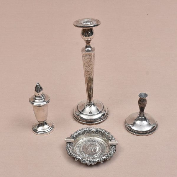 Quatro peças de prata de diferentes procedências e decorações: Castiçal lavrado em acantos (alt. 21 cm), cinzeiro português todo cinzelado (diam. 10 cm) e saleiro e base de castiçal. Peso com breu 500