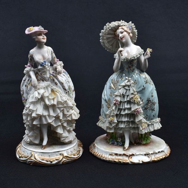 Par de estatuetas de porcelana italiana representando figuras de damas da corte com trajes típicos da corte com saias rendilhadas. Alt. 19 e 20 cm. Uma delas com pequenas imperfeiçoes nos rendilhados