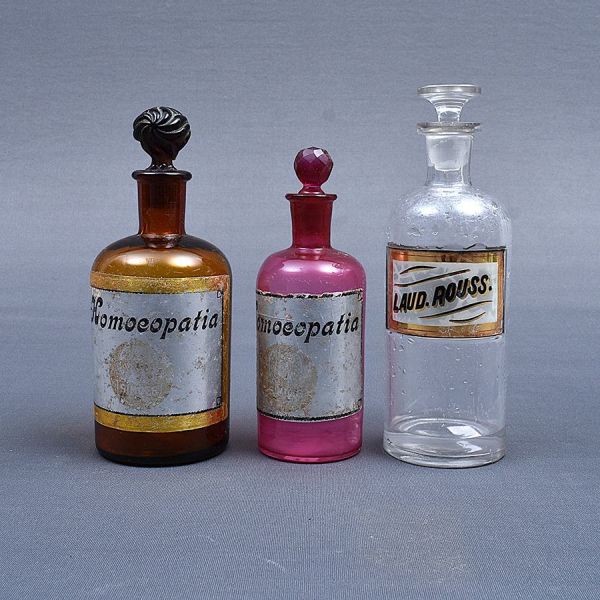 Três antigos potes de farmacia do sec. XIX de vidro: Um na cor fumê inscrição `Homoeopatia`, outro tranlúcido `Laud. Rouss. E o terceiro na cor rosa inscrição `Homoeopatia`. Alt. 21, 22 e 18 cm.