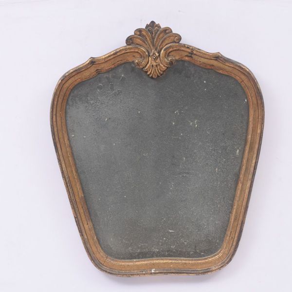 Espelho estilo Louis Philippe com moldura em madeira dourada, de contorno arredondado e perfil canelado simples encimada por discreto motivo de concha estilizada . Med. 71 x 60 cm.