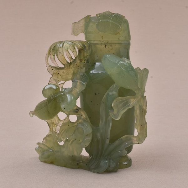 Escultura chinesa do sec. XIX em jade verde entalhada representando uma urna com flores entalhadas. Alt. 16 cm. Pequenas perdas pontuais nos elementos florais da base e da tampa.