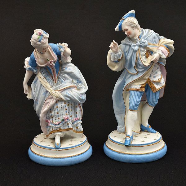 Par de estatuetas de biscuit alemão na predominância da cor azul com detalhes policromados representando casal de figuras da corte. Alt;. 26 e 24 cm. Ambos com restauro no pescoço.