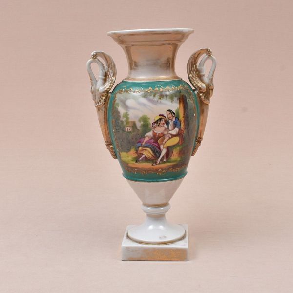 Ânfora francesa Vieux paris de porcelana. Decoração em reserva com cena de galanteio em policromia. Alças com detalhes em dourado representadas por cisnes estilizados. Alt. 33 cm.
