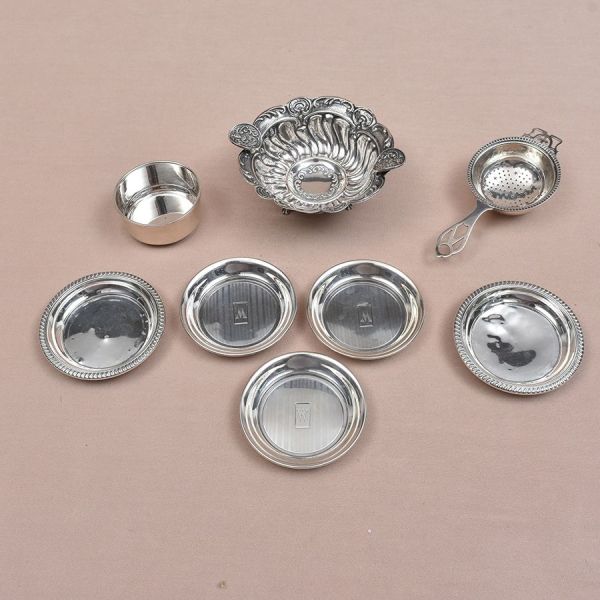 Sete peças de prata de diferentes procedências e decorações: Cinco saleiros, coador de chá de prata inglesa e cinzeiro todo cinzelado (diam. 10 cm). Peso total da prata 235g.