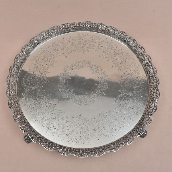 Bandejão redondo de prata brasileira e marca do prateiro Michel Kouri. Centro lavrado em acantos e borda cinzelada no mesmo padrão. Pés de garras. Diam. 52 cm. Peso: 3.295g.