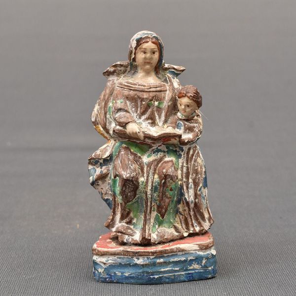 Brasil – sec. XIX. Miniatura de imagem em madeira policromada representando de Santana sentada com Nossa Senhora ensinando a menina a ler em seu livro sagrado. Alt. 10 cm.