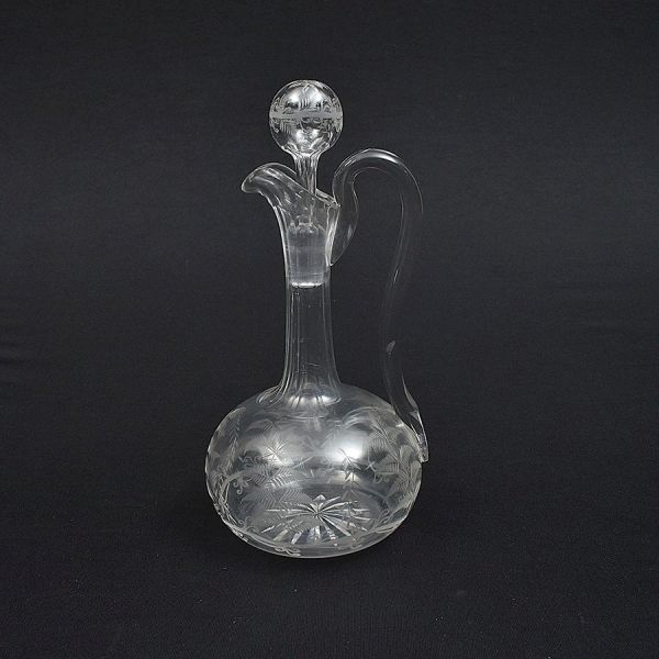 Licoreira francesa de cristal translúcido lavrado com folhagem. Alça em elegante movimento. Apresenta um quebradinho no encontro da alça com bojo. Alt. 28 cm.