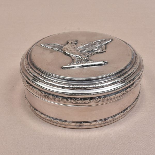 Porta joias prateado europeu de formato circular com figura de galo cinzelado em relevo. Detalhes de folhagens de louro em anéis. Diam. 15 cm.