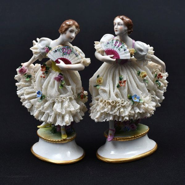 Par de estatuetas de porcelana alemã representando figuras de damas com saias filigranadas. Alt. 14 cm. Pequenos quebradinhos na saia