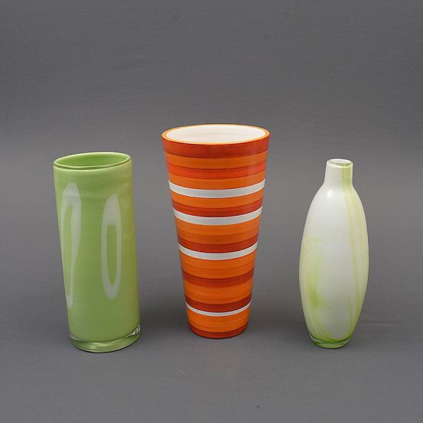 Três vasos de cristal, sendo um degradê em faixas na cor vermelho alaranjado e os outros dois verdes com branco. Alt. 33, 30, 30 cm.
