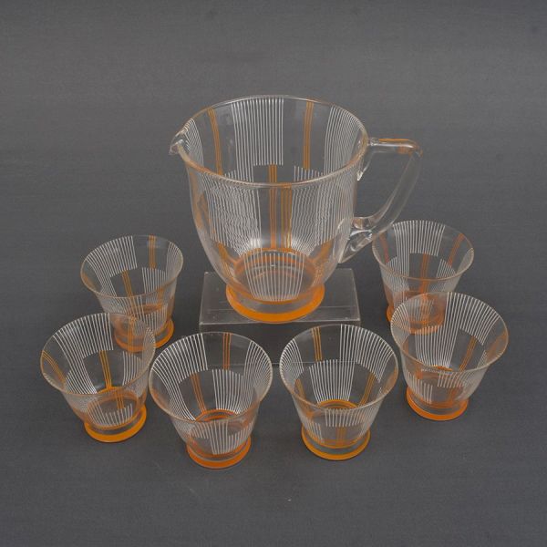 Jarra com 6 copos de cristal europeu decorados em frisos verticais em branco e laranja sobre fundo translúcido. Alt. 16 e 8 cm.