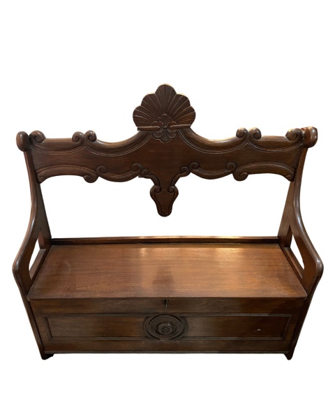 Banco colonial em madeira de lei maciça com encosto alto ornamentado por entalhes barrocos. O assento articulado funciona como tampa para um amplo baú inferior, equipado com fechadura e chave original.