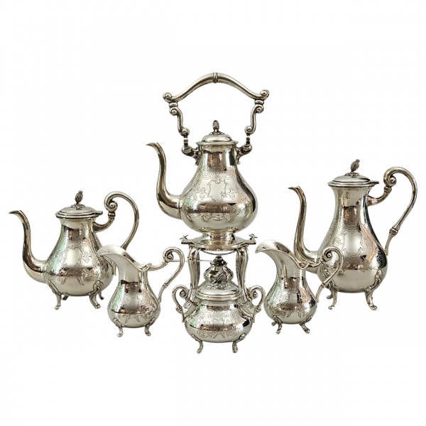 Belo serviço de prata teor 833, sobre pés elevados, decorado com incisões vegetais, circunfluindo reserva em branco, composto de: 1 bule para chá, 1 bule para café, 1 leiteira, 1 cremeira, 1 açucareir