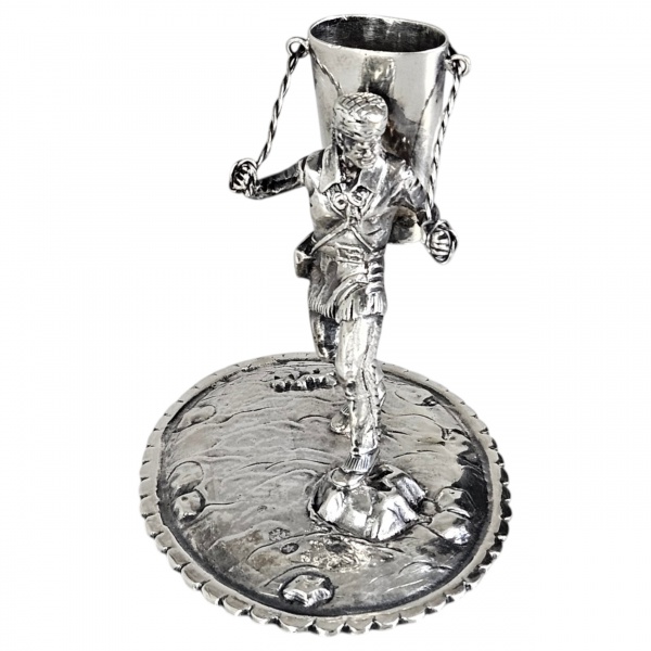 Paliteiro de prata, moldada e cinzelada, estilo naturalista, representando figura masculina em trajes campestres, sustentando cesto destinado a acondicionamento de palitos. Base oval de metal espessur