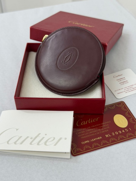 Carteira de Moedas Cartier Must de Cartier. Dimensões aproximadas: 10 cm de largura x 9,5 cm de altura. Confeccionada em couro granulado na cor bordô, possui fechamento por zíper e logotipo Cartier em