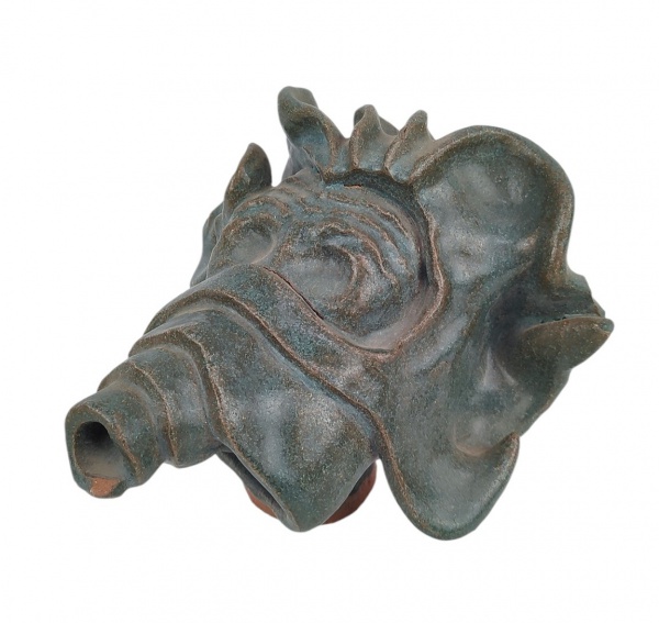 Escultura em barro cozido, pintada na cor verde, representando "Cabeça de figura estilizada". Apresenta dois lascadinhos e discretas fissuras de fabricação. Med. 15x18,5x17,5cm.