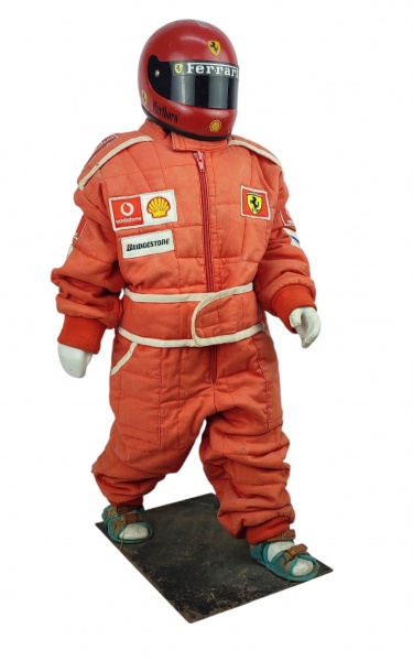 Boneco decorativo em material sintético, com macacão infantil de Fórmula 1 e capacete em fibra. Apresenta desgastes causados pelo tempo. Alt. 71cm.