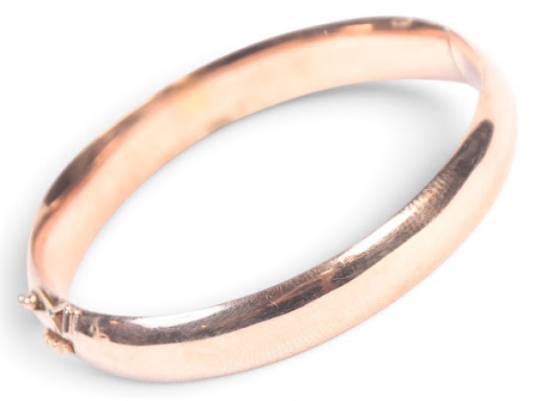 PULSEIRA / BRACELETE RÍGIDO ARTICULADO EM OURO ROSÉ / OURO BAIXO: Clássico e elegante bracelete feminino rígido de formato ovalado com secção de meia-cana convexa, executado em ouro rosé com acabamento exterior liso espelhado e discretas estrias finas acetinadas ao longo do aro; estrutura articulada por charneira central traseira com abertura total, provida de fecho oculto de encaixe tipo gaveta com botão de pressão e fecho exterior de segurança basculante em forma de oito/alça metálica;  peça em bom estado geral de conservação, exibindo estrutura firme, fecho e charneira funcionais e suaves marcas/micro-riscos superficiais condizentes com o uso. Medida 6 cm de diâmetro . Peso 13,8 g