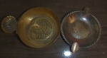 Dois objetos de metal, sendo um cinzeiro de prata com 20 g com dois descansos e outro de metal dourado da Portico com descanso em forma de concha, ao centro com brasão.