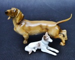 BASSET e RUSKY SIBERIANO. Dois cachorros de porcelana: um na cor marrom e o outro branco com mesclas na cor marrom. Medidas: 8,5 x 13,5 cm e 4 x 7,5 cm.