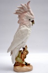 ROYAL DUX SÉCULO XX  - Escultura de porcelana tcheca na cor branco e rosa,  representando cacatua pousada em tronco de árvore. Marca da manufatura no fundo da peça. Altura 41 cm.