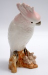 ROYAL DUX BOHEMIA ( FINAL DE  1947-1990) - Escultura de porcelana  Theca,  na cor branco e rosa,  representando pássaro pousado em tronco de árvore . Marca da manufatura no fundo da peça. Altura 18 cm.