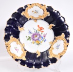 MEISSEN SÉCULO XX - Medalhão de porcelana policromada azul da Prússia com cartelas brancas emoldurada a ouro, decoração floral. Diâmetro 30 cm.