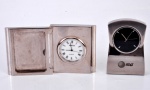 Dois relógios de mesa de cabeceira em metal prateado, mecanismo quartzo. Alturas 5,5 e 6 cm.