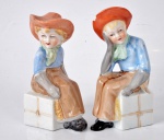 Duas estatuetas de porcelana representando crianças com chapéu ( um deles com quebrado). Marcado Vieira de Castro.