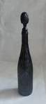 Antiga garrafa licoreira confeccionada em vidro prensado antigo na cor fumê, lapidado, com tampa adaptada em vidro prensado na cor azul cobalto. Med.: 34 cm