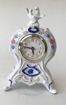 Relógio de mesa com estrutura de porcelana (sem marca) na tonalidade branca e desenhos decorativos em azul, folhagens e flores em alto relevo (maquinário a pilha) aprox. 25 x 14 x 9 cm