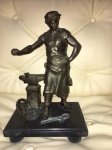 ALEGORIA AO TRABALHO- Escultura em bronze, representando guerreiro com bigorna e ferramentas apoiada sobre uma base de mármore negro. Med: 30 x 17 sem base. Com a base 34 x 23 x 16 cm