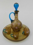 Lote com cinco peças sendo uma bandeja redonda, uma jarra e três cálices de cristal âmbar e azul decorado com relevo de galhos e flores.