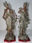 Par de esculturas de petit bronze, na figura de jovens com ramos de flores nas mãos, sobvre base de madeira. Mede 60 cm altura cada.