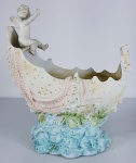 Antiga floreira europeia em porcelana biscuit policromado, realçado com gotículas duradas, representando barco com anjinho sobre o mar. Altura 22 cm, comprimento 20 cm e largura 11 cm.