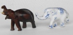 2 Elefantes sendo um esculpido em madeira (indiano), medindo: 5,5 cm x 4 cm e outro em porcelana chinesa, medindo: 5,5 cm x 3 cm, com uma perna quebrada.