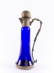 Belíssima e antiga jarra tipo decanter em vidro na cor azul cobalto e guarnições em metal trabalhado, e tampa esférica cinzelada. Med.: 37 x 17 cm.