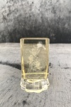 Peso de papel em vidro  âmbar lapidado 3D com decoração interna de querubins  apoiado sobre pé em vidro translucido com bordas onduladas. Med:  0,08 x 0,05 x 0,05 cm.